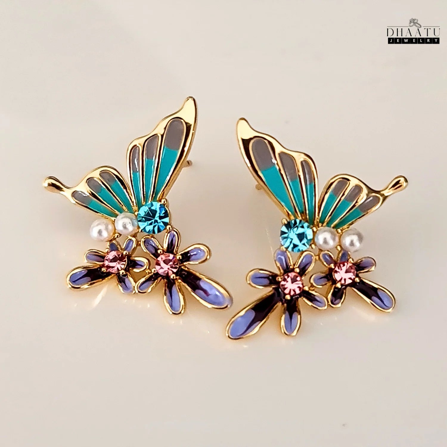 Pair of turquoise and purple butterfly and flower stud earrings with a white background.
