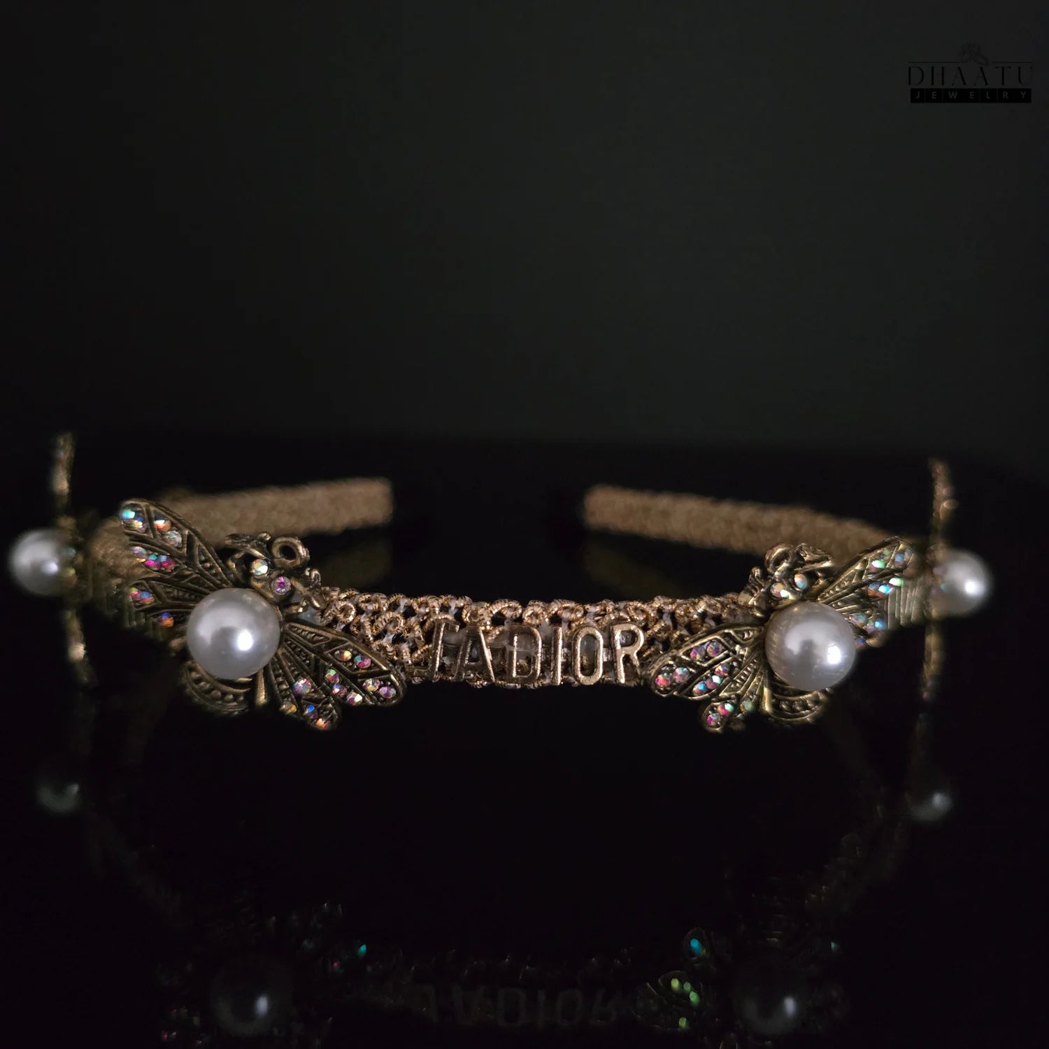 Elegant golden designer inspired headband with bee and pearl embellishments, presented against a dark background for dramatic effect.