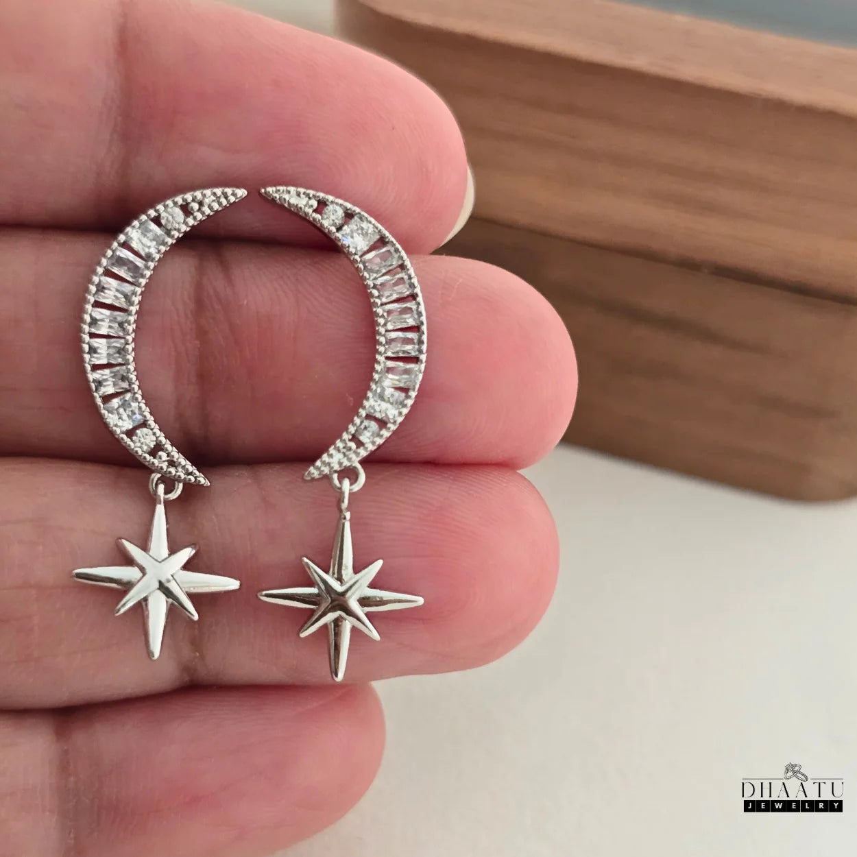 Close-up of zircon-encrusted moon and star dangle earrings held in a hand, highlighting intricate details and sparkle