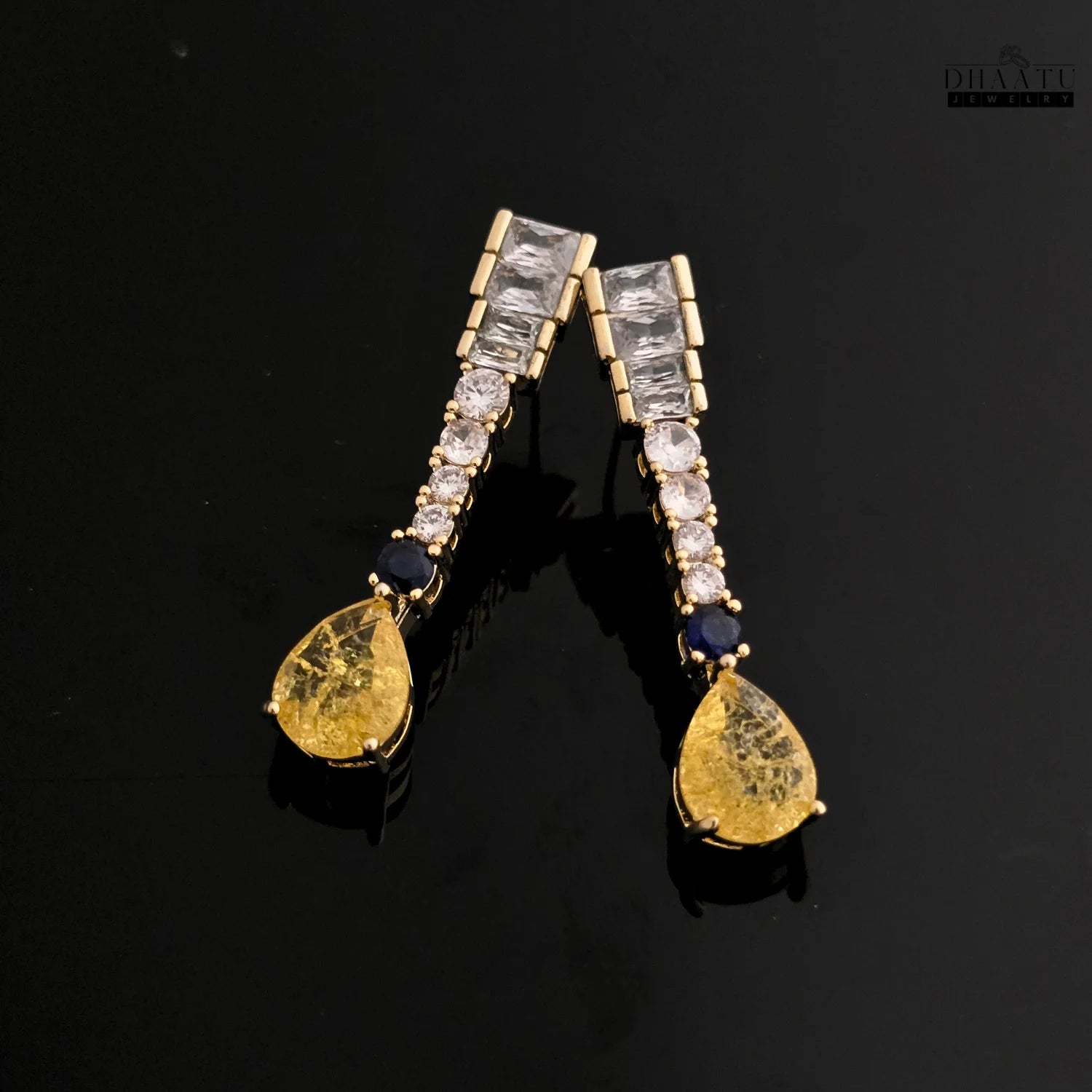 Gold-toned Zircon drop earrings with yellow and blue stones against a glossy black background