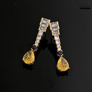 Gold-toned Zircon drop earrings with yellow and blue stones against a glossy black background