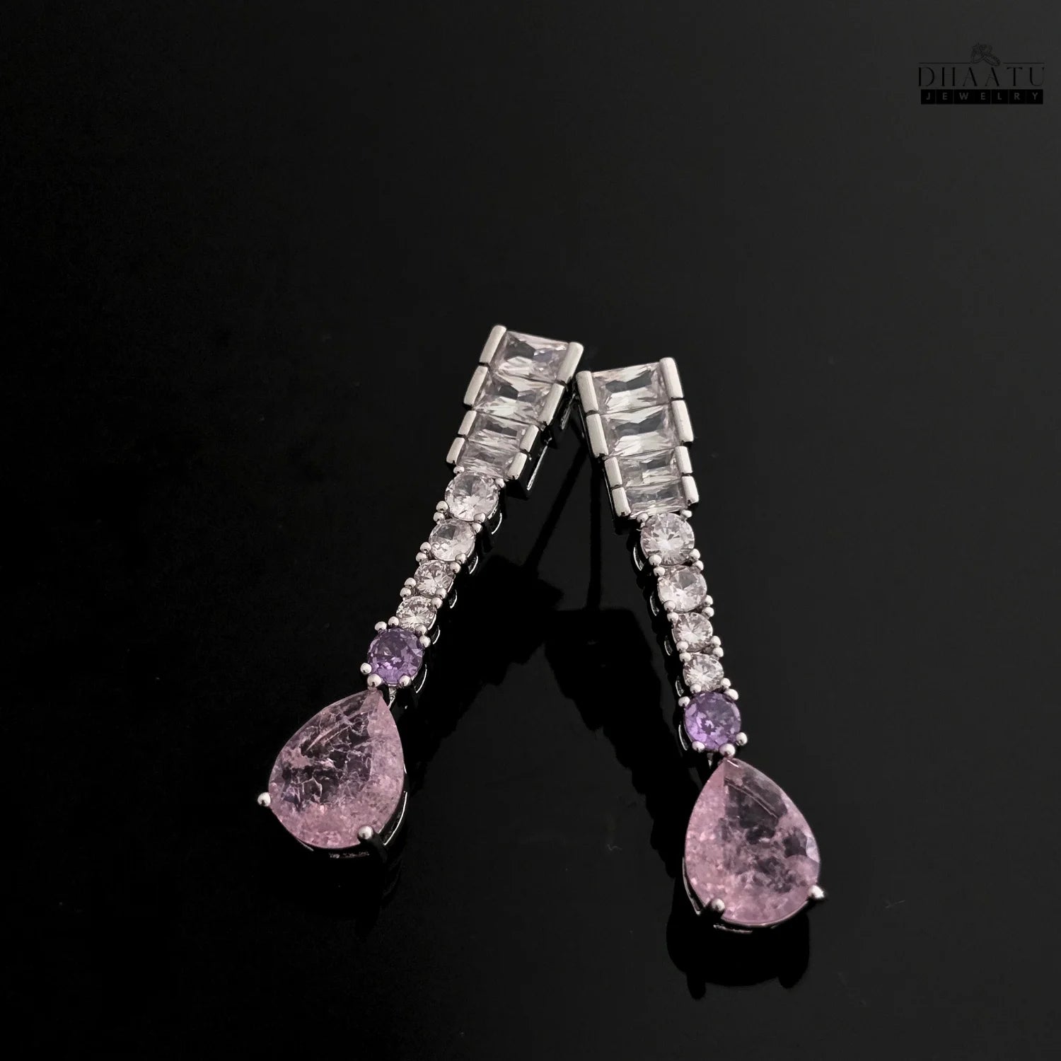 Silver-toned Zircon drop earrings with pink and lilac stones on a glossy black background