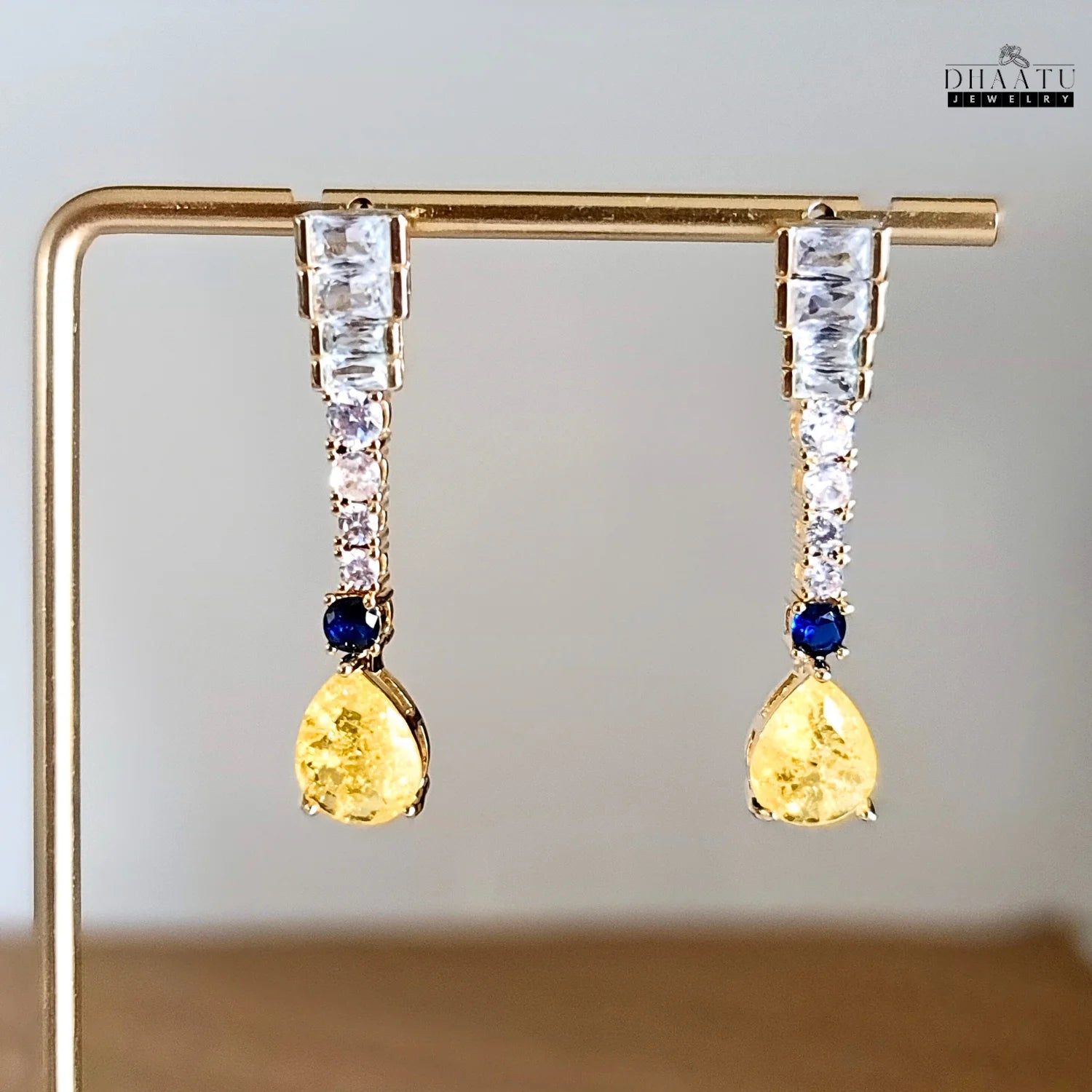 Close-up shot of gold-toned Zircon drop earrings with yellow pear-cut and blue round stones