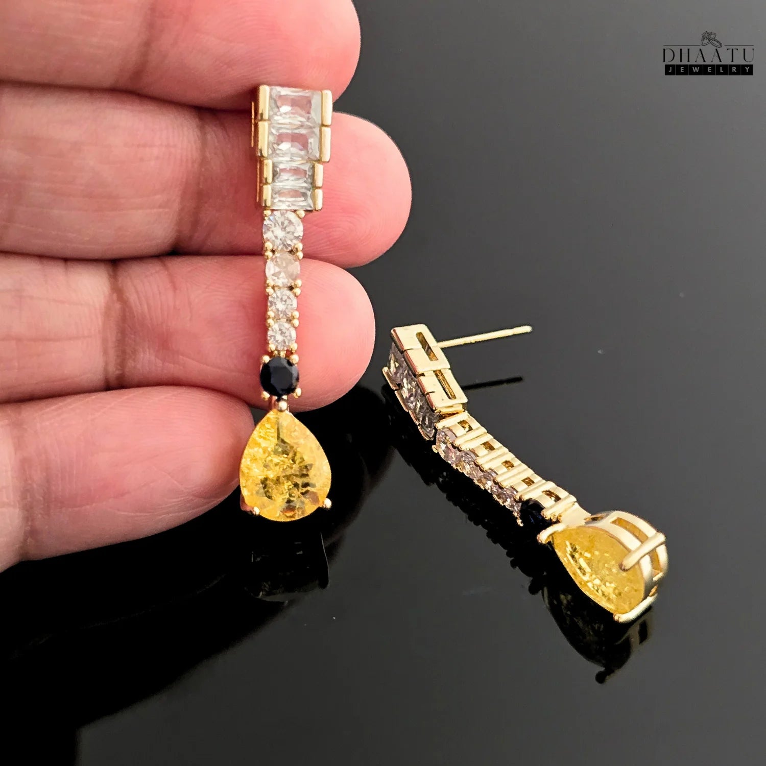 Hand holding a single gold-toned Zircon drop earring with yellow pear-cut and blue round stone