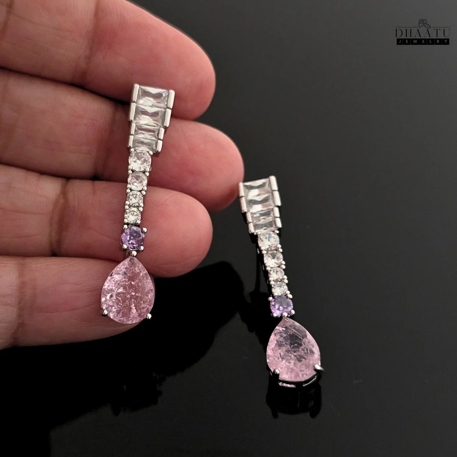 Hand holding a single silver-toned Zircon drop earring with pink pear-cut and lilac round stone