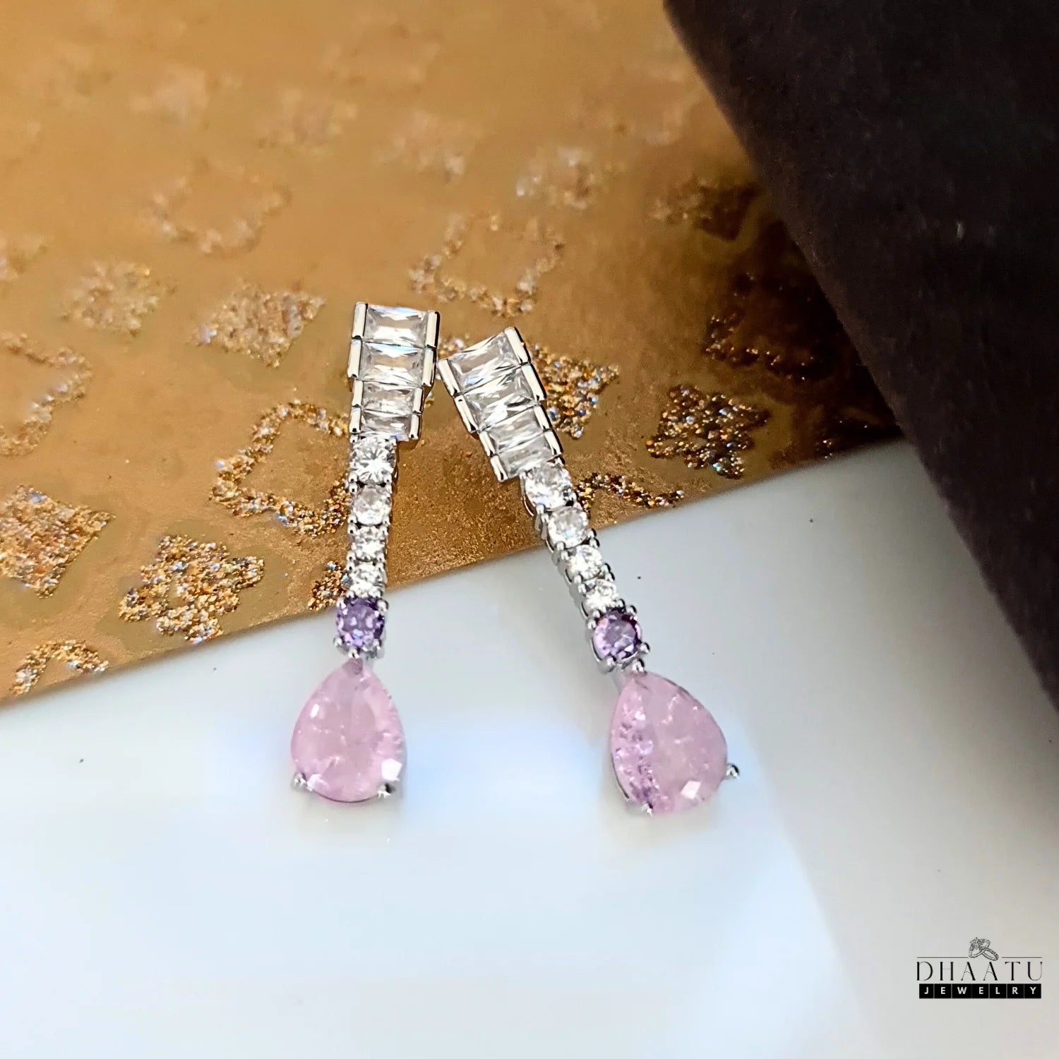 Pair of silver-toned Zircon drop earrings with pink pear-cut and lilac round stones on a textured gold background