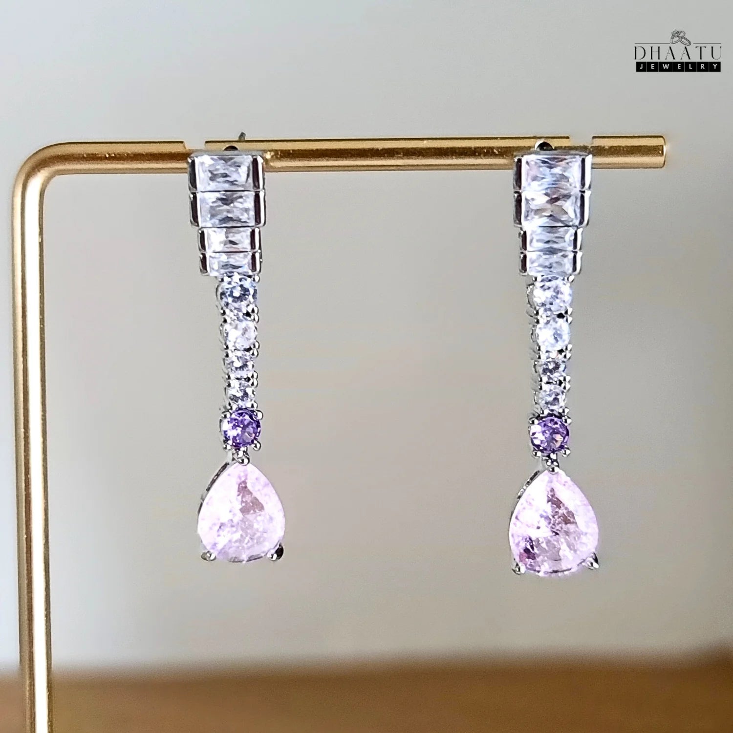Silver-toned Zircon drop earrings with pink and lilac stones on a light-colored, textured surface