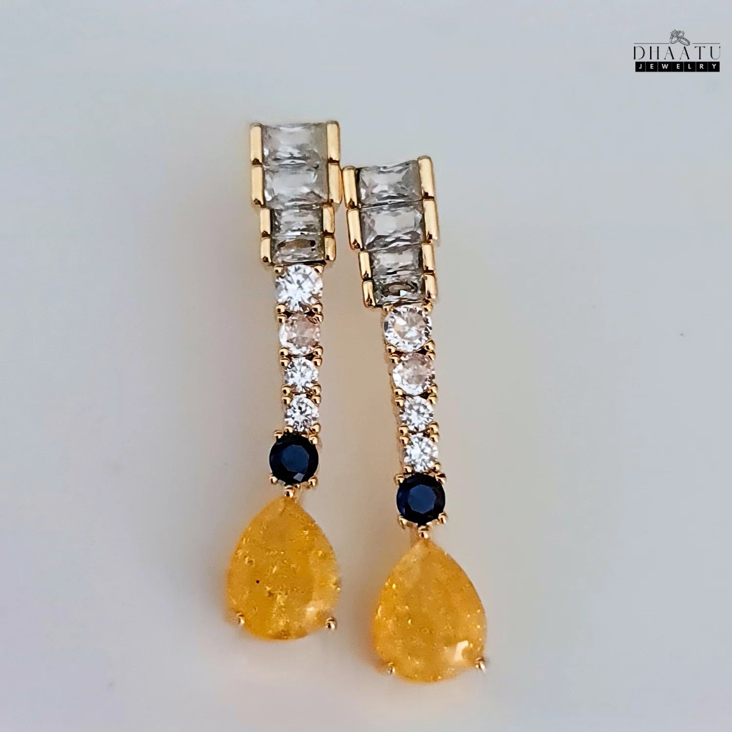Top view of gold-toned Zircon drop earrings with yellow and blue stones on a white background