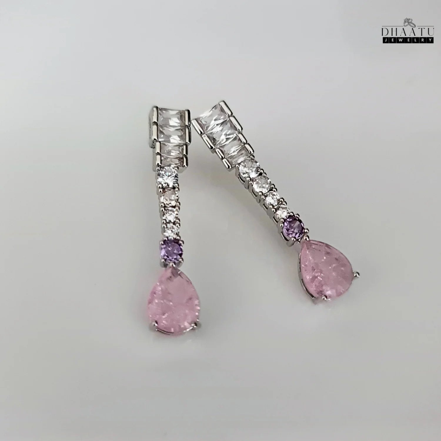 Top view of silver-toned Zircon drop earrings with pink and lilac stones on a white background